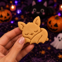 Cute sleeping bat Halloween cookie held in front of a spooky pumpkin and bat party background