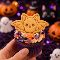 Flying Chibi Bat cookie on a decorated Halloween cupcake with orange, purple, and cream frosting, held in a hand against a spooky party background.
