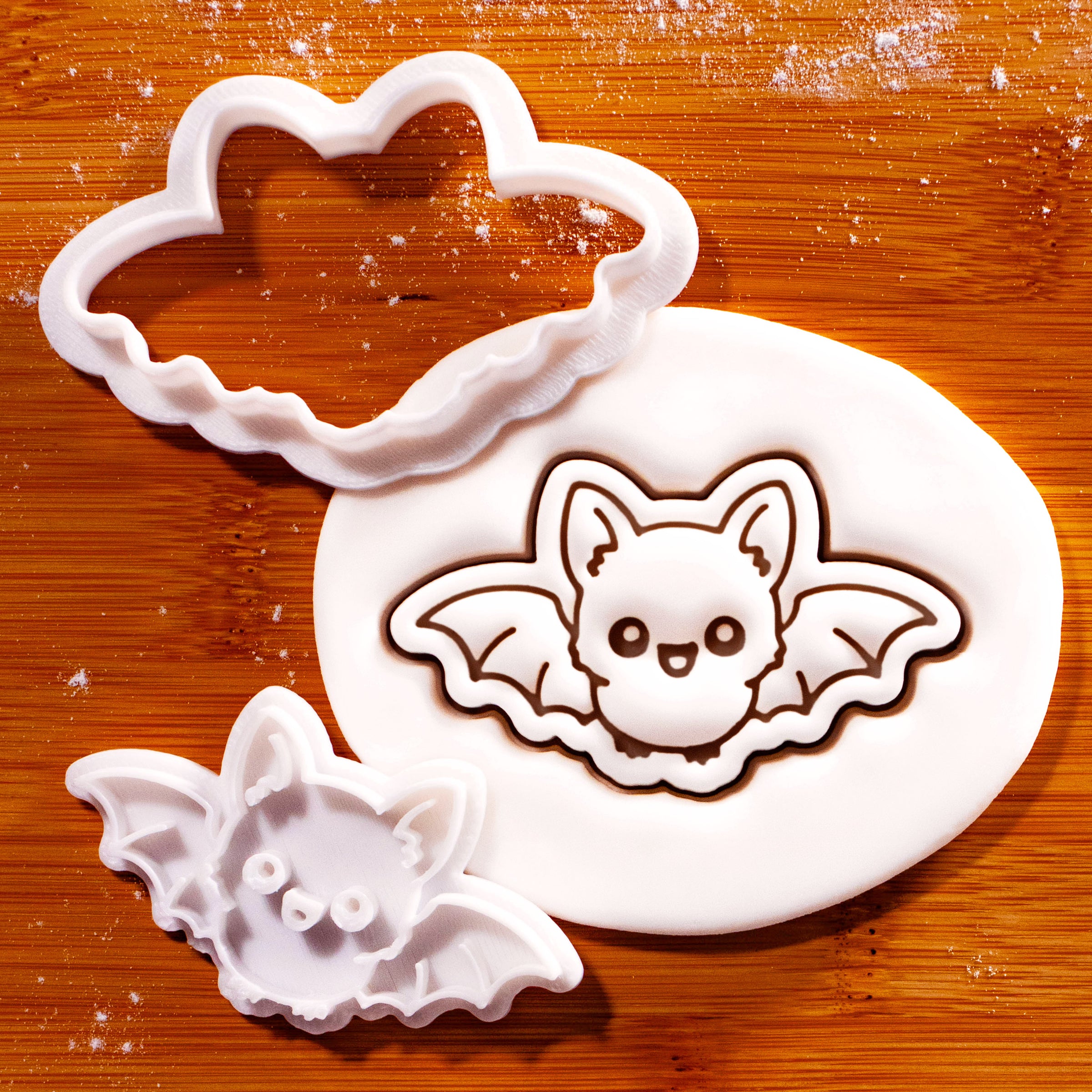 Flying Chibi Bat Mini Cookie Cutter and matching stamp set displayed on a wooden surface beside rolled white fondant embossed with a cute flying bat design.
