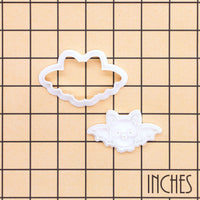 Flying Chibi Bat Mini Cookie Cutter and stamp set shown on an inch grid background to display the size of the Halloween baking tools.