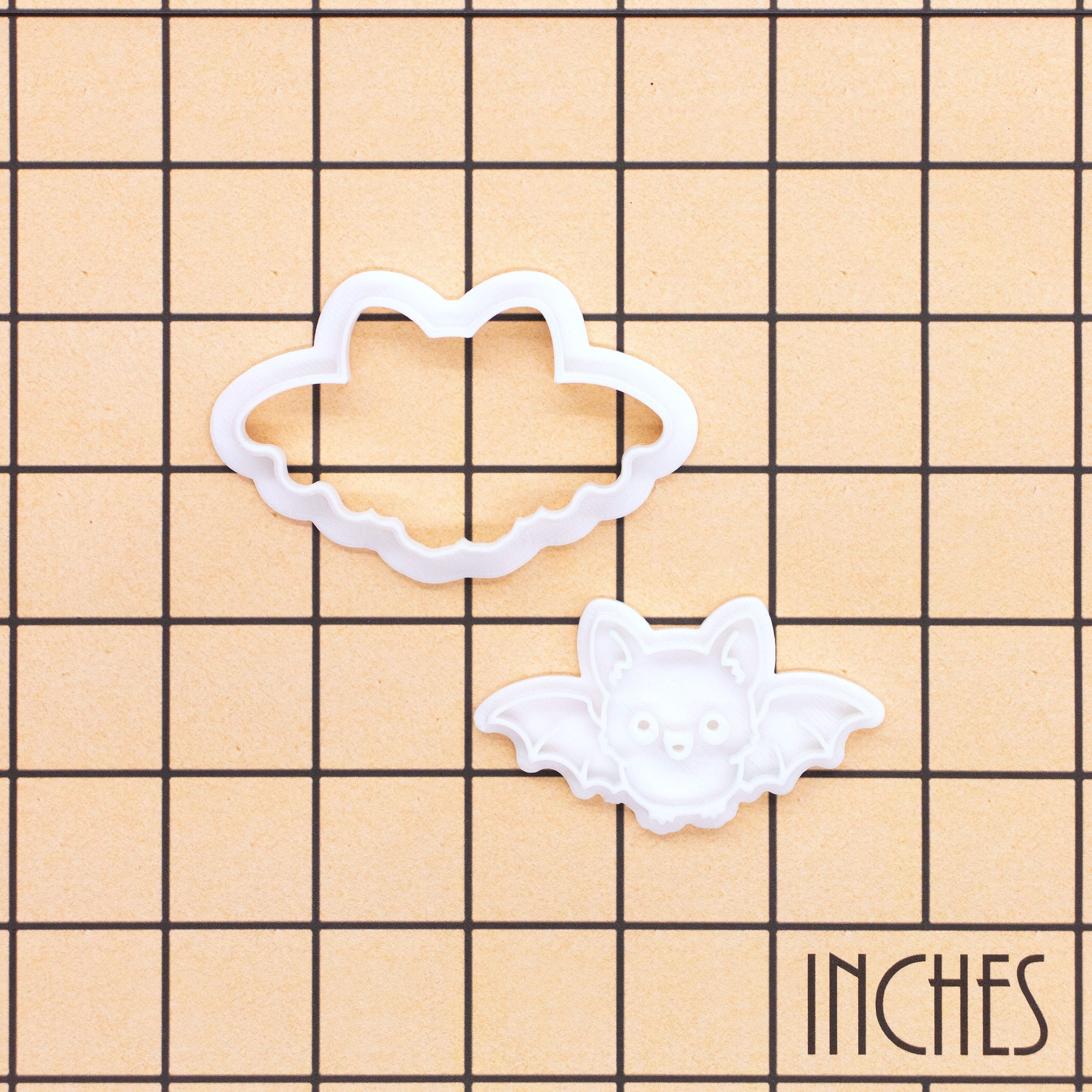 Flying Chibi Bat Mini Cookie Cutter and stamp set shown on an inch grid background to display the size of the Halloween baking tools.