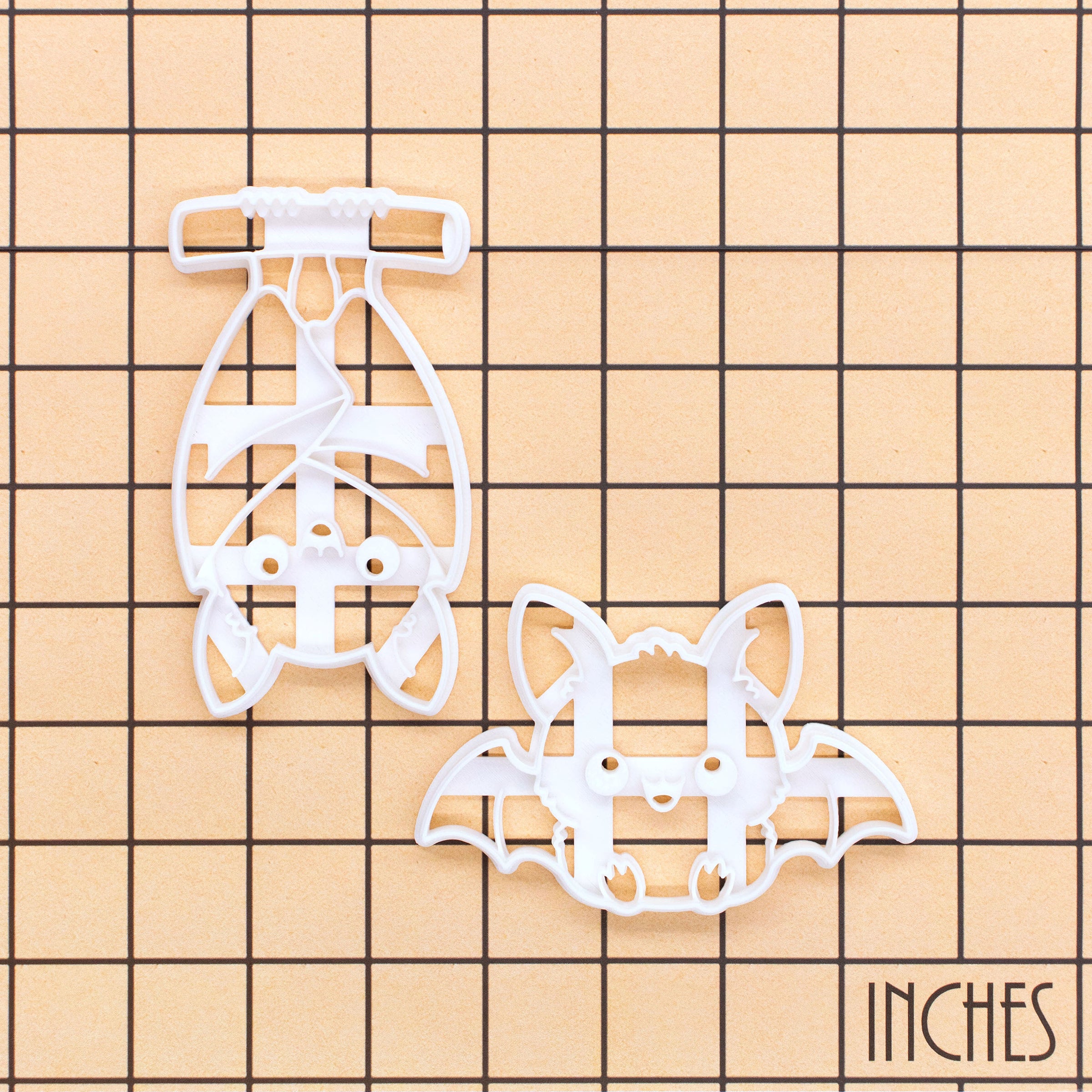 Sitting and hanging chibi bat Halloween cookie cutters shown on an inch measurement grid for size reference