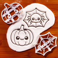 Chibi spider web and kawaii pumpkin cookie cutters beside detailed fondant impressions