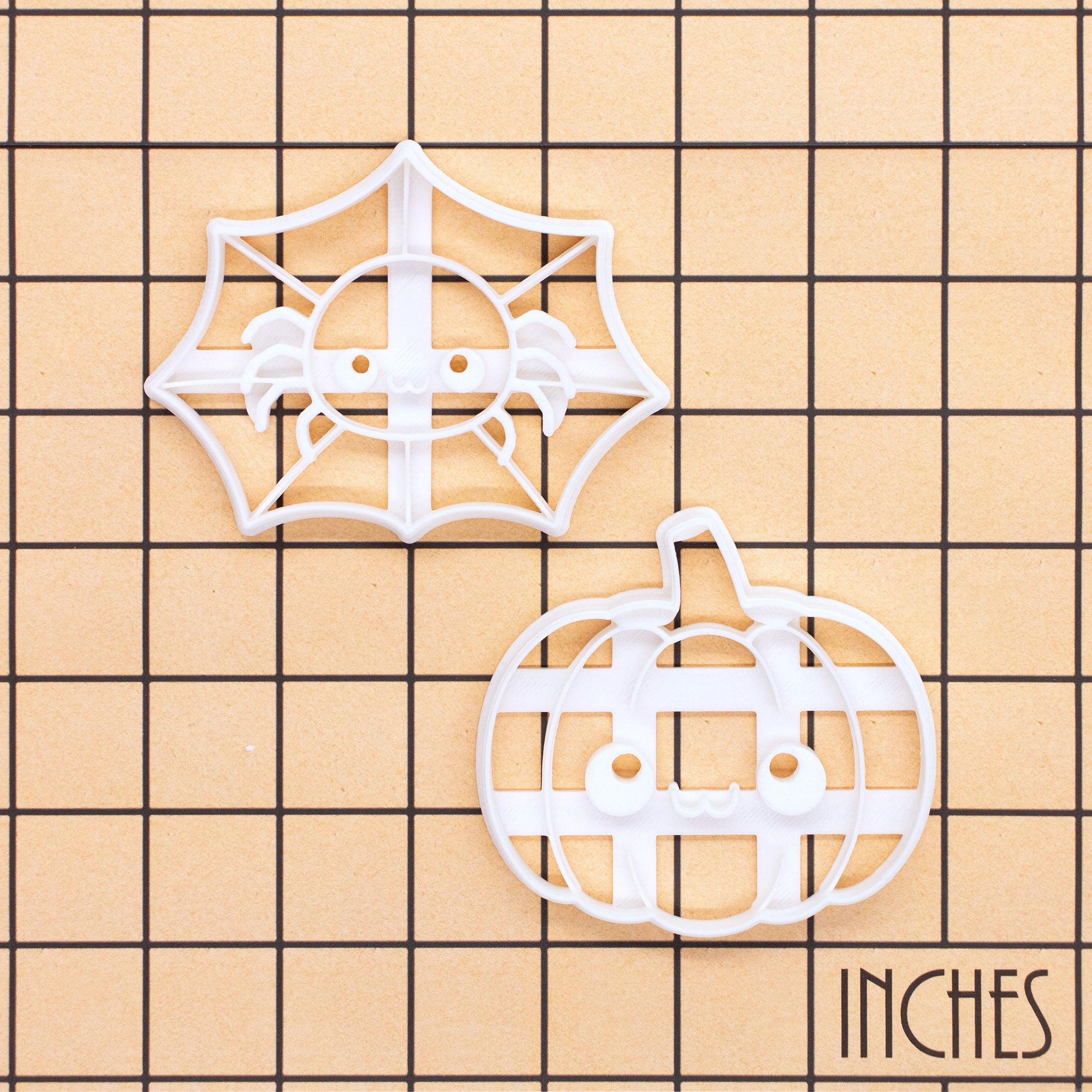 Spider web and pumpkin cookie cutters shown together on an inch measurement grid