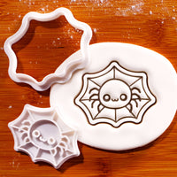 Chibi spider in web mini cookie cutter beside a fondant impression on a wooden board
