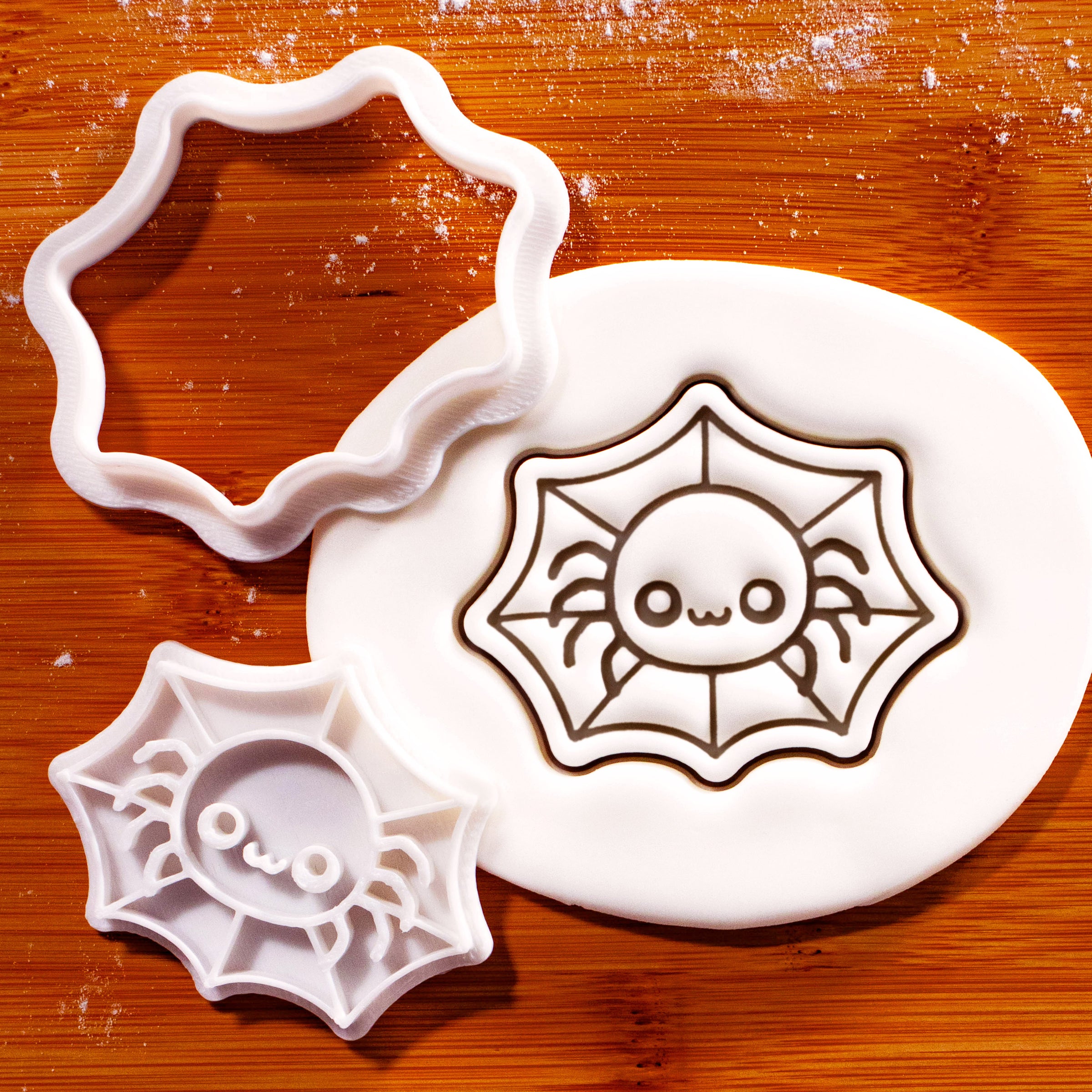 Chibi spider in web mini cookie cutter beside a fondant impression on a wooden board