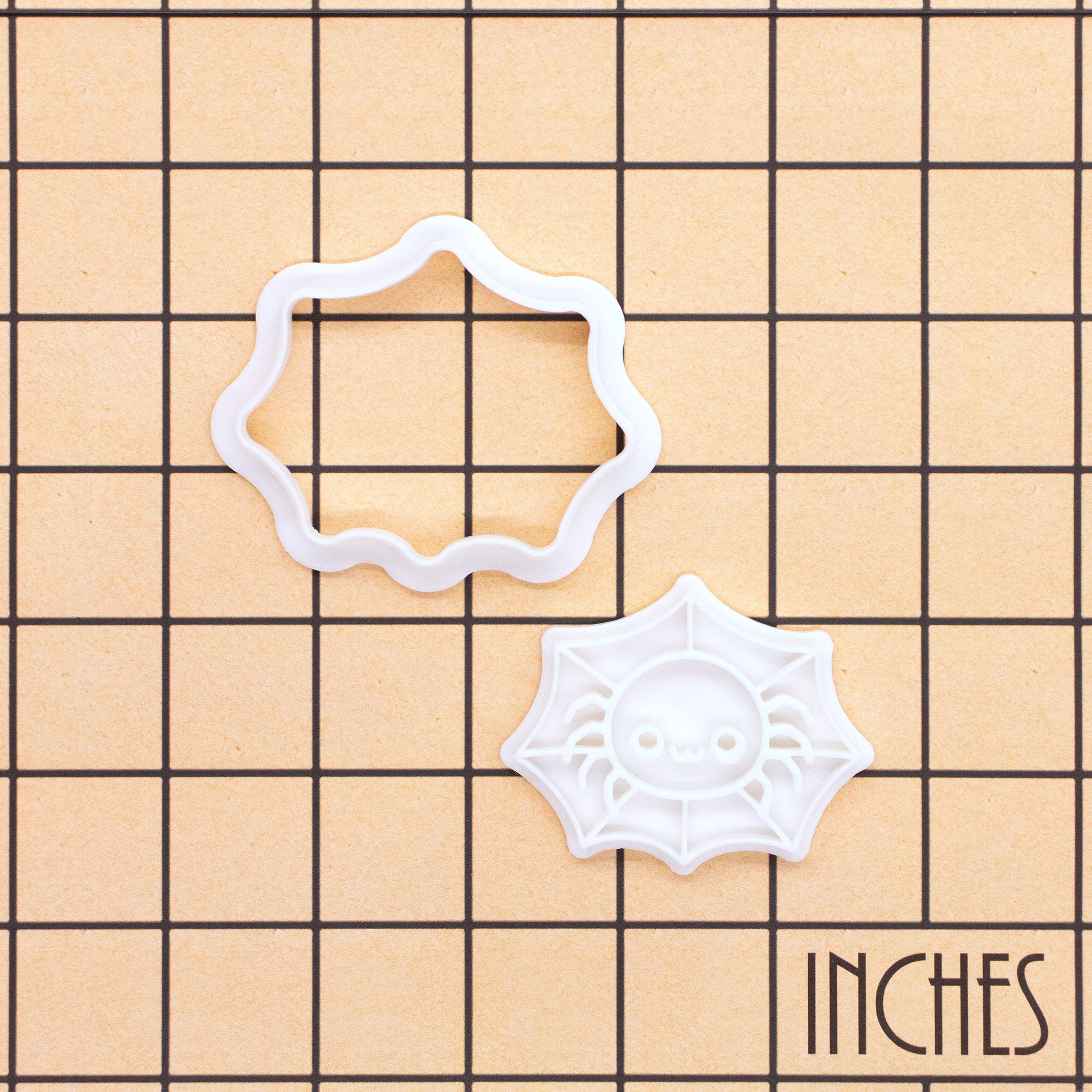 Chibi spider in web mini cookie cutter shown on an inch measurement grid
