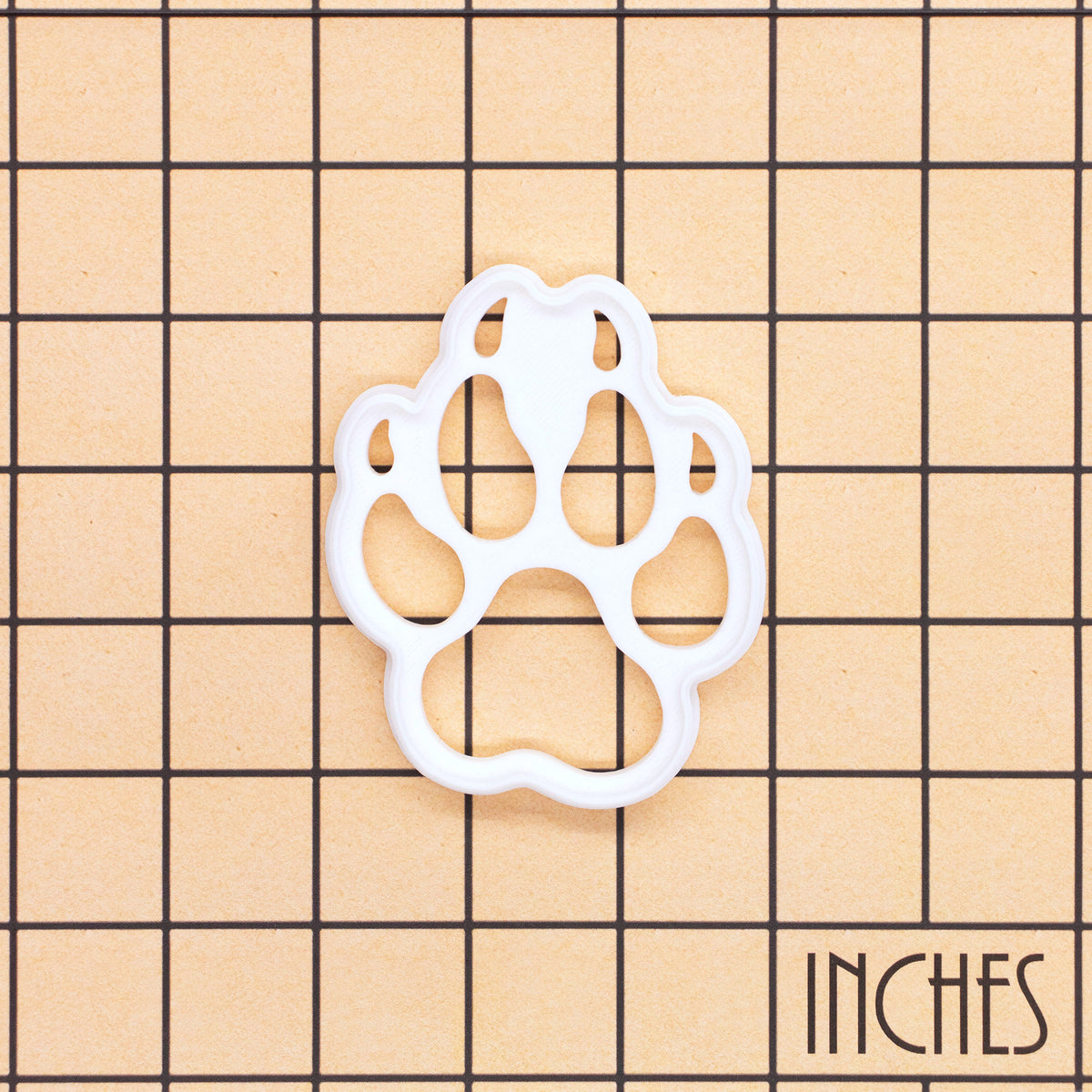 Wolf paw print mini cookie cutter and stamp shown on inch measurement grid