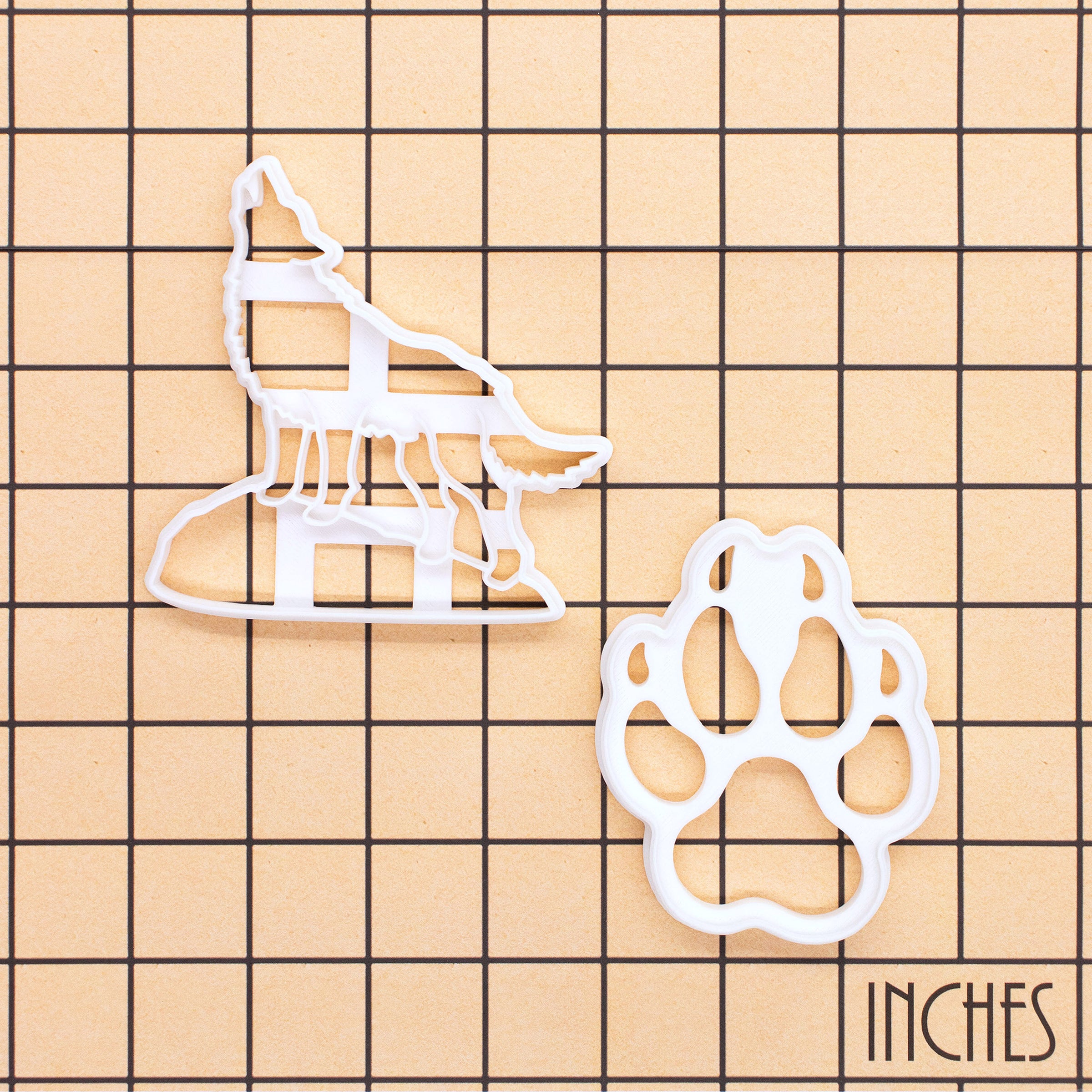 Set of two howling wolf and wolf paw print cookie cutters on inch grid