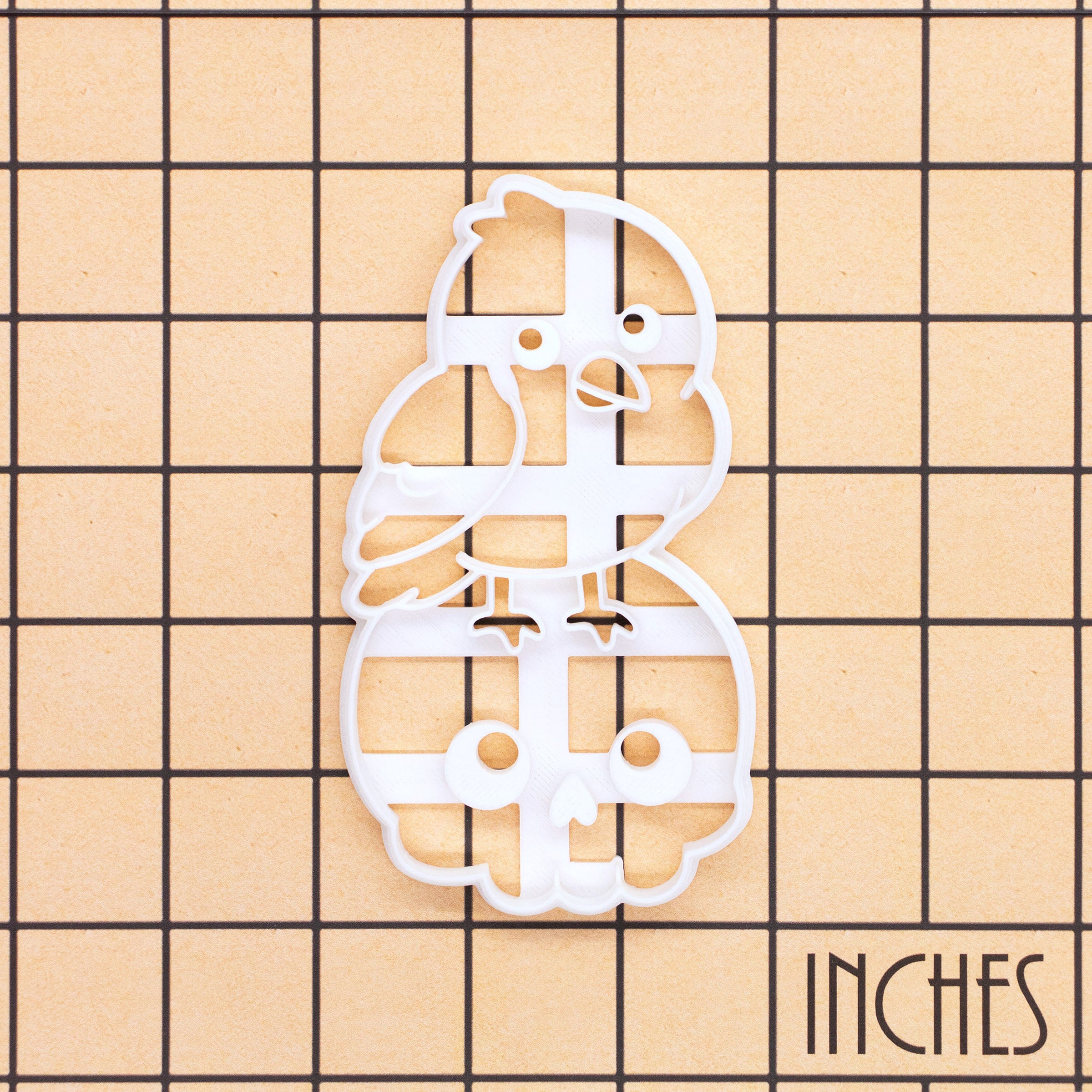 Kawaii raven on skull Halloween cookie cutter shown on an inch measurement grid