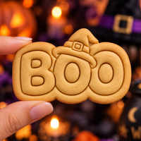 BOO witch hat embossed Halloween cookie held by hand against a blurred witch-themed background
