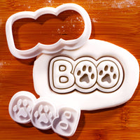 BOO Paw Print Mini Cookie Cutter and separate stamp set shown with clear impression in white fondant on a wooden surface