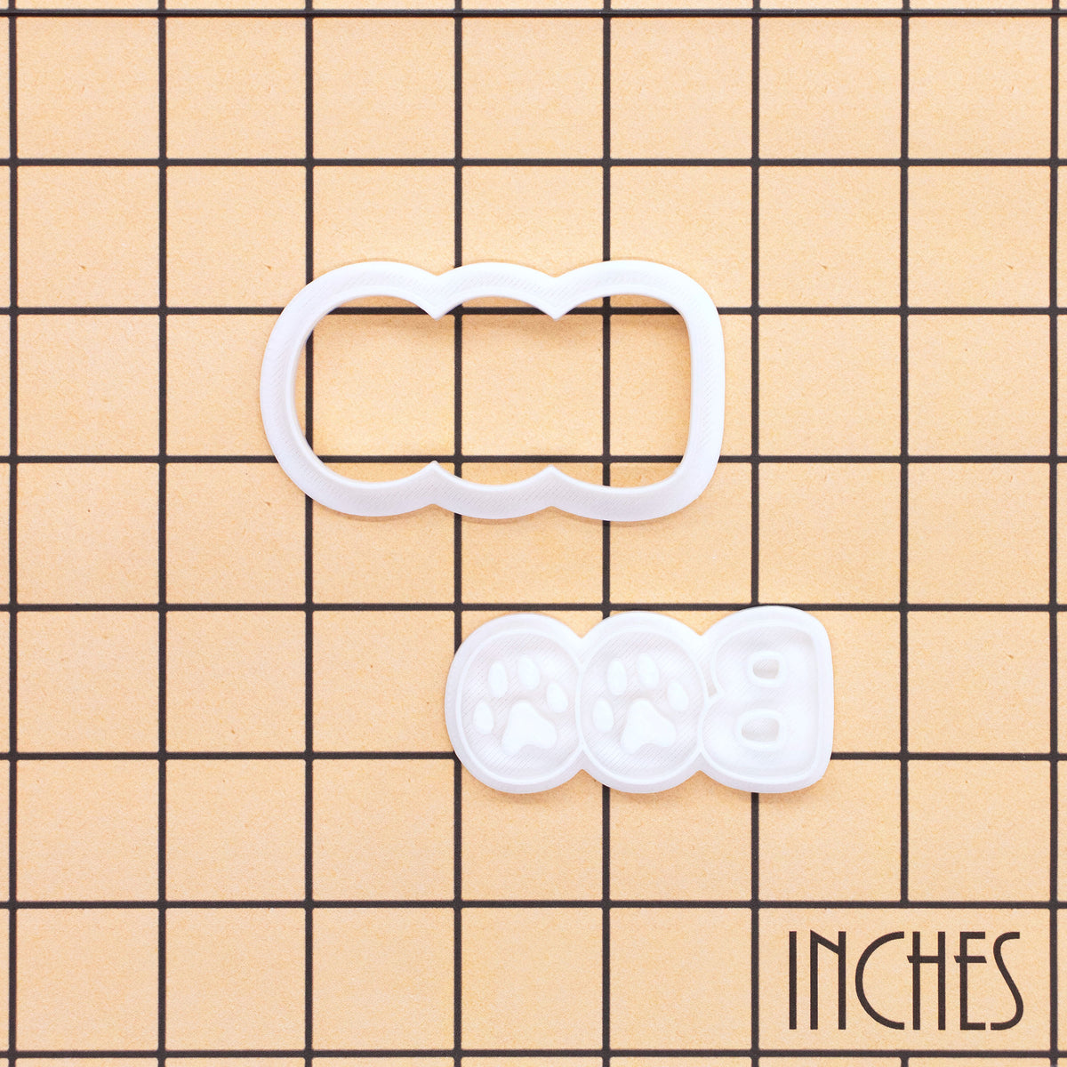 BOO Paw Print Mini Cookie Cutter and separate stamp displayed on an inch measurement grid