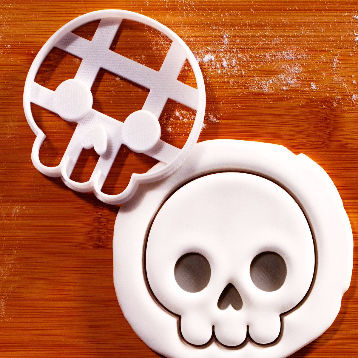 Cute Skull front view cookie cutter beside a detailed skull impression in white fondant on a wooden baking surface