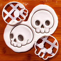 Set of 2 cute skull cookie cutters with front and side view skull impressions in white fondant on a wooden board