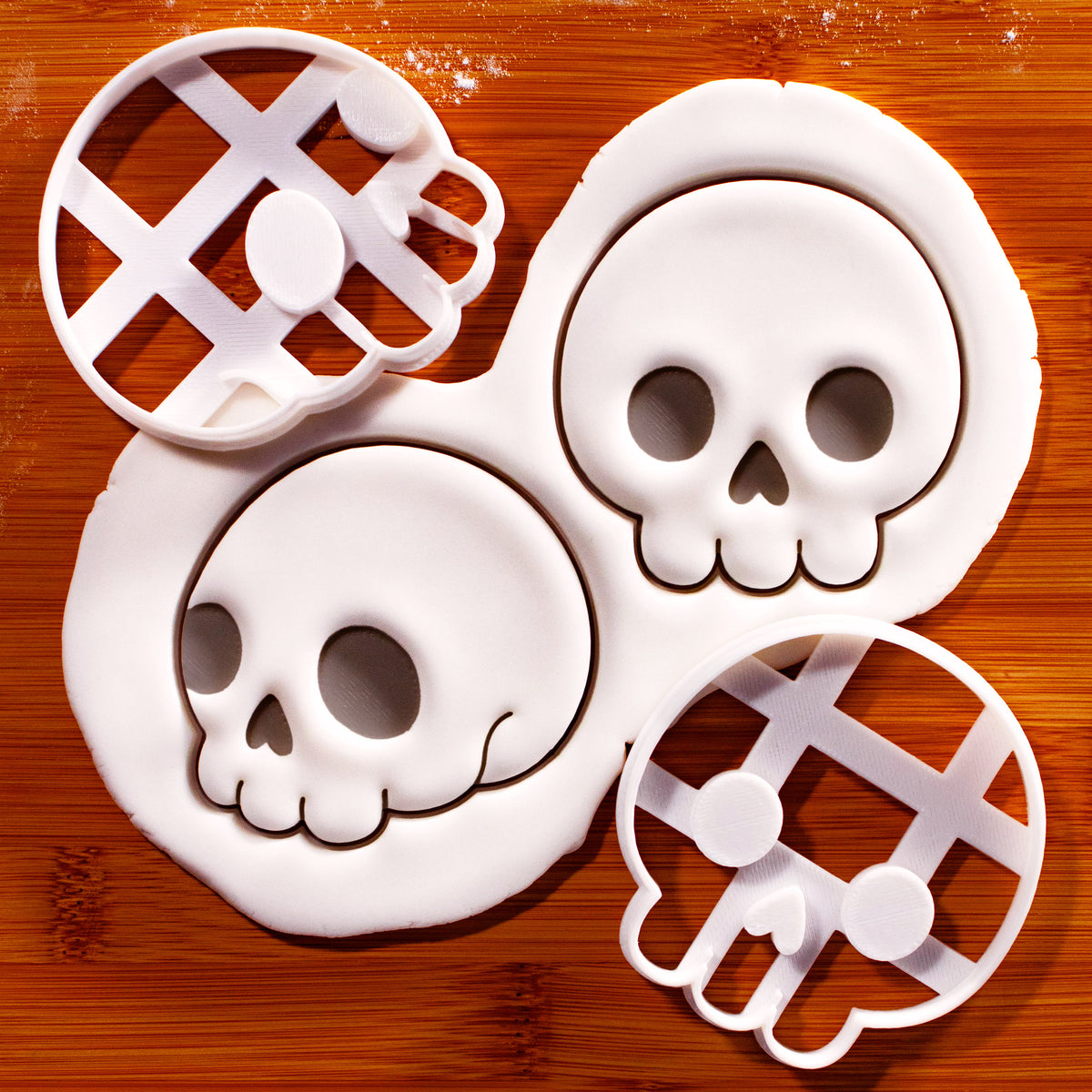 Set of 2 cute skull cookie cutters with front and side view skull impressions in white fondant on a wooden board