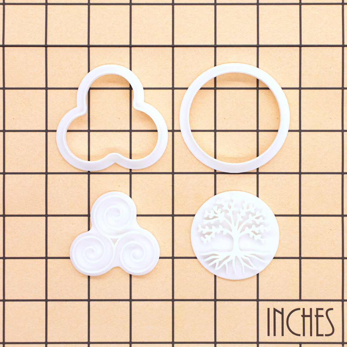 Tree of Life and Triskelion mini cookie cutter and stamp pieces displayed on inch measurement grid