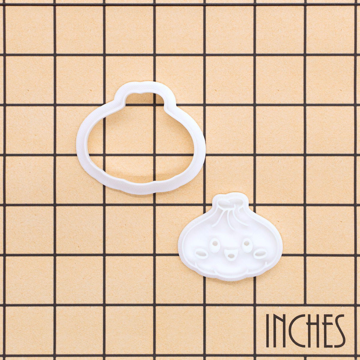 Mini dumpling cookie cutter and smiling Xiao Long Bao stamp shown on inch measurement grid