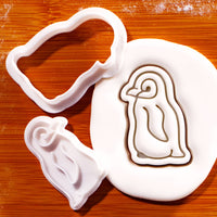 Baby penguin mini cookie cutter and detailed stamp beside embossed sugarpaste penguin impression