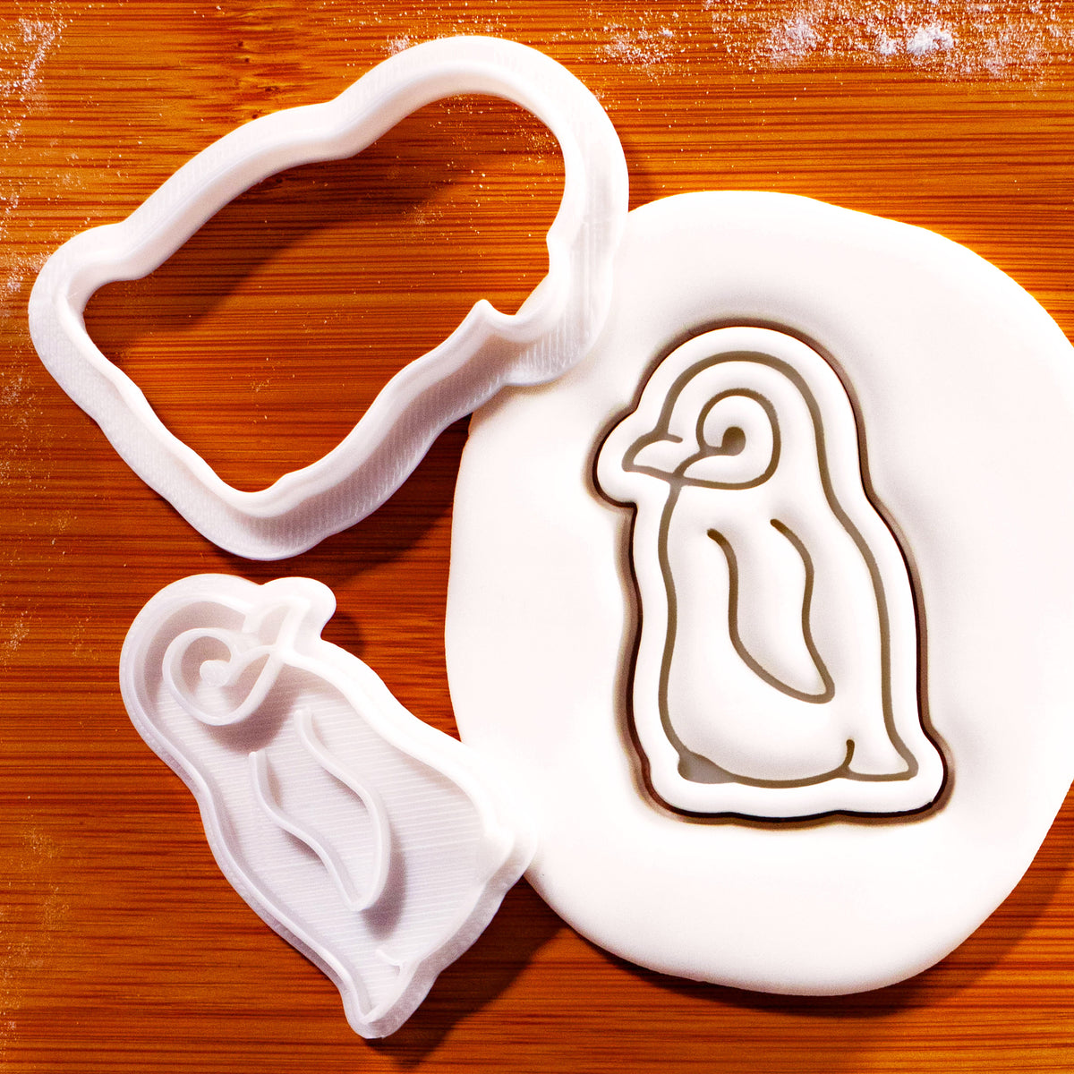 Baby penguin mini cookie cutter and detailed stamp beside embossed sugarpaste penguin impression