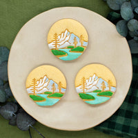 mountain with pine tree forest cookies with royal icing rivers and grassy hills, and hand painted mountains with edible food coloring